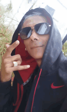 a man wearing sunglasses and a black nike hoodie giving the peace sign