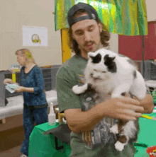 a man is holding a black and white cat in his arms while a woman looks on