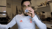 a man wearing an adidas shirt drinks from a cup