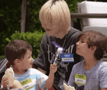 a boy with a name tag that says ' hello ' on it is holding a wand and talking to two young boys .