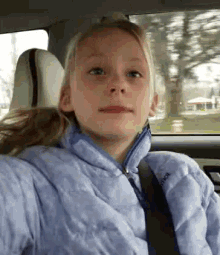 a young girl is sitting in the back seat of a car with a seat belt around her neck .