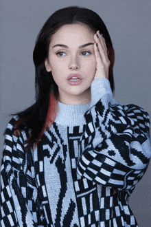 a woman wearing a black and white sweater is covering her face with her hand