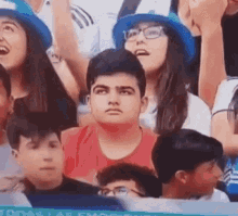 a group of people are sitting in a stadium watching a game . one of the people is wearing a blue hat .