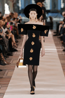 a model walks down a runway wearing a black dress