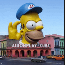 a giant statue of homer simpson wearing a blue hat is in front of a building that says alronplay de cuba