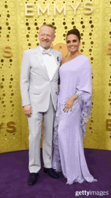 a man in a suit and a woman in a purple dress pose on a purple carpet at emmy awards