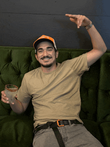 a man sitting on a couch holding a drink and wearing a hat that says ny