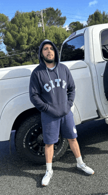 a man in a city hoodie stands in front of a truck