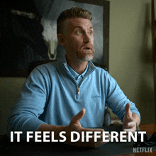 a man in a blue shirt is sitting at a desk with the words " it feels different " above him