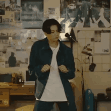 a young man in a blue jacket is dancing in a room with posters on the wall .