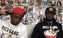 two men wearing rice gang shirts are standing in front of a wall full of magazines