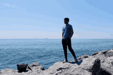 a man standing on a rock near the ocean with his hands in his pockets