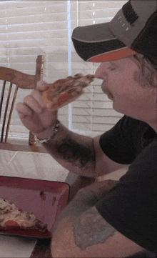 a man is eating a slice of pizza and wearing a hat that says ' a ' on it