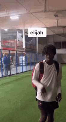 a man with a backpack is walking on a soccer field in a gym .