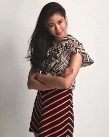 a woman with her arms crossed wearing a striped skirt and a patterned top