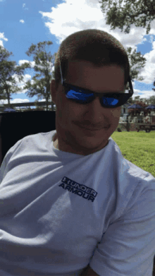 a man wearing sunglasses and a white under armour shirt smiles