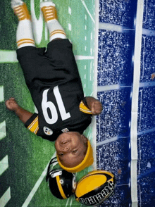 a baby in a pittsburgh steelers jersey is laying upside down on the field