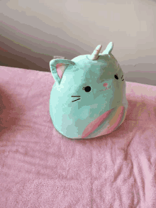 a stuffed cat with a unicorn horn is sitting on a pink blanket