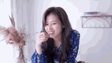 a woman in a blue dress is sitting at a table with a vase of dried flowers in front of her