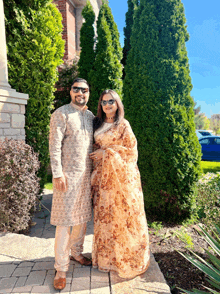 a man and a woman pose for a picture in front of some trees