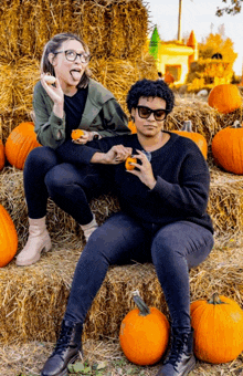 a man and a woman sitting on a pile of hay eating pumpkins