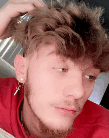 a young man with a beard is wearing a red shirt and silver earrings