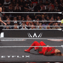 a woman in a red outfit is laying on the ground in a wrestling ring with netflix written on the floor