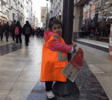 a little girl in an orange vest is holding a newspaper that says izmir