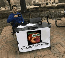 a man sits behind a table with a sign that says change my mind