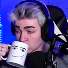 a man wearing headphones is drinking from a coffee mug with a face on it .