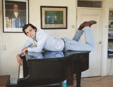 a man laying on top of a piano with his legs crossed