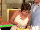 a woman in a white dress is cutting a piece of food in front of a sign that says rocks