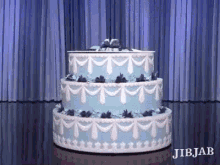 a blue and white cake is on a table in front of a blue curtain