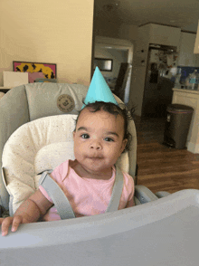 a baby sitting in a high chair wearing a blue party hat