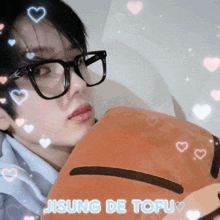 a young man wearing glasses is holding a stuffed animal with the words jisung de tofu written below it