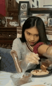 a young girl is sitting at a table with a bowl of food and a spoon in her hand .