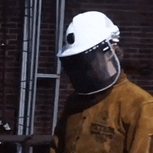 a man wearing a hard hat and a beekeeper 's suit is standing in front of a brick wall .