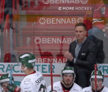 a man in a suit talks to a group of hockey players in front of a banner that says ' c more hockey '