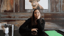 a woman sits at a desk with her hand on her face and a picture of a cow on the wall behind her