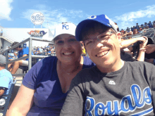 a woman wearing a kc hat sits next to a man wearing a gray royals shirt