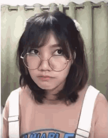 a girl wearing glasses and overalls is making a face .