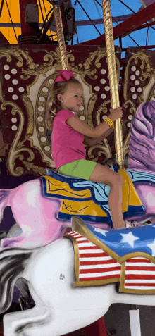 a little girl is riding a pink and white carousel horse