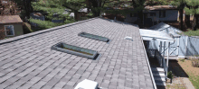 a roof with three skylights on it and a house in the background