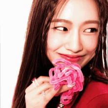 a woman in a red shirt is holding a pink flower in her hand