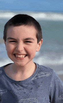 a young boy wearing a blue shirt with cars on it smiles