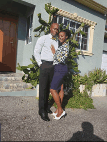 a man and woman pose for a photo in front of a house