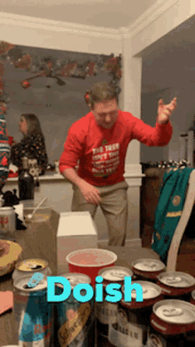 a man in a red sweater is dancing in front of a table full of beer cans with the word doish on it