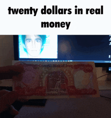 a person holding a twenty dollar bill in front of a computer