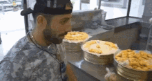 a man wearing a hat is standing in front of a counter with a bunch of cakes on it .