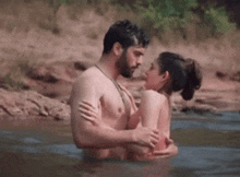 a shirtless man and a naked woman are hugging in a river .